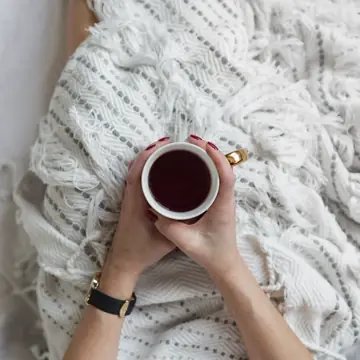 Battaniye altında iki elle tutulan sıcak bir fincan
